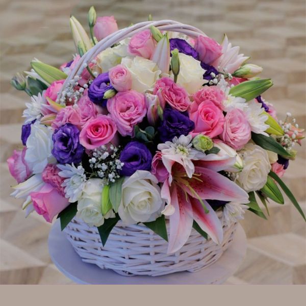 Mixed-Floral-Gift-Basket/ A white basket overflowing with a mix of pink and purple blooms, white roses, and pink lilies.