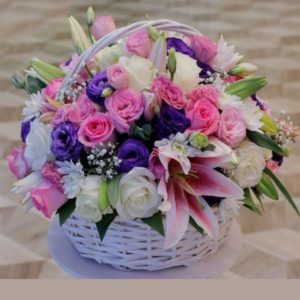 A white basket overflowing with a mix of pink and purple blooms, white roses, and pink lilies.